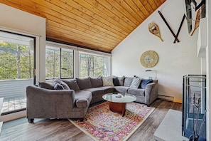A modern living room with a wooden ceiling, a large window, a sectional sofa, a coffee table, and a decorative clock. - Spectacular Mountain View Condo: Aquatic Facility & Ski Shuttle (Lincoln)