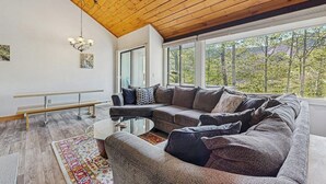 A modern living room with a wooden ceiling, large windows, a sectional sofa, and a glass coffee table. - Spectacular Mountain View Condo: Aquatic Facility & Ski Shuttle (Lincoln)