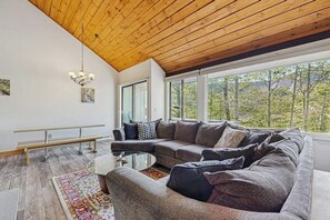 A modern living room with a wooden ceiling, large windows, a sectional sofa, and a glass coffee table. - Spectacular Mountain View Condo: Aquatic Facility & Ski Shuttle (Lincoln)