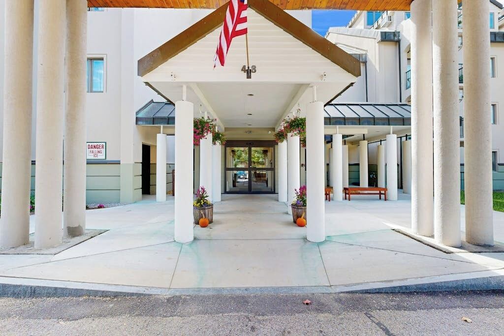 A covered entrance with columns, a flag, and a sign indicating a falling ice hazard.
