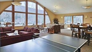 Una habitación amplia con mesa de ping pong, asientos cómodos, ventanas grandes y chimenea.