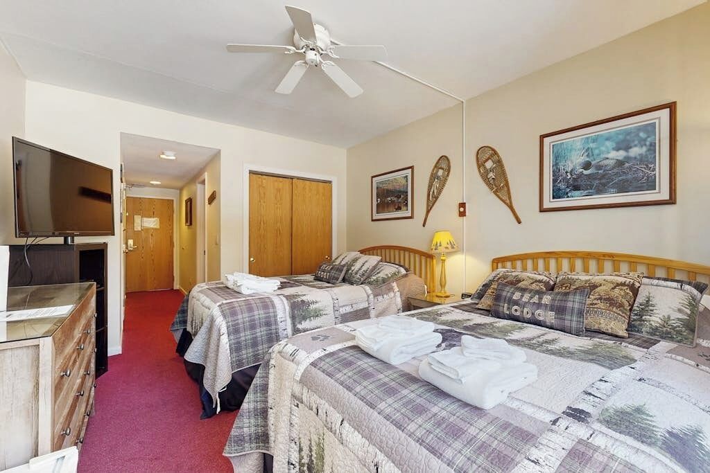A bedroom with two beds, a ceiling fan, a TV, and a wooden wardrobe.
