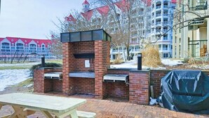 Zona de barbacoa de ladrillo con mesa y bancos, rodeada de edificios.