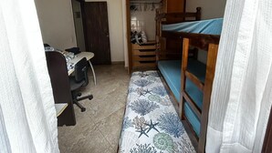 Una habitación pequeña y funcional con literas, un escritorio con silla y un armario.