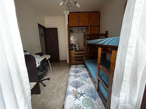 Ein kleiner, kompakter Raum mit Etagenbett, Schreibtisch und Stuhl sowie einem Kleiderschrank.