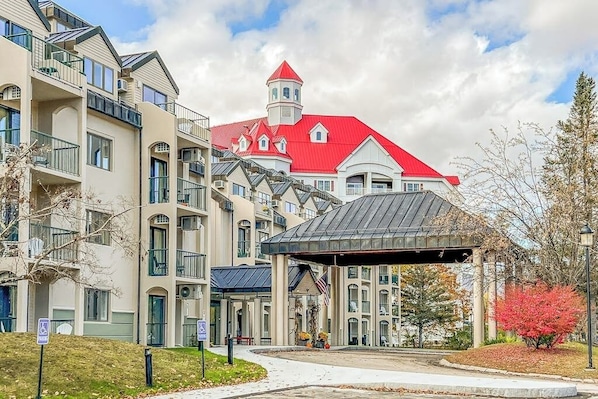 A multi-story hotel with a red-roofed building, a covered entrance, and a parking area. - Mountainside condo w/ pool, gym & rec room:  walk to ski lift & town (Lincoln)