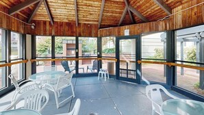 A covered patio area with tables and chairs, large windows, and a wooden ceiling. - Mountainside condo w/ pool, gym & rec room:  walk to ski lift & town (Lincoln)