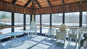 A covered outdoor seating area with tables and chairs, large windows, and a wooden ceiling. - Mountainside condo w/ pool, gym & rec room:  walk to ski lift & town (Lincoln)