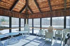 A covered outdoor seating area with tables and chairs, large windows, and a wooden ceiling. - Mountainside condo w/ pool, gym & rec room:  walk to ski lift & town (Lincoln)
