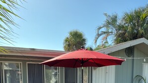 Een terras met een tafel en stoelen, een rode parasol en een bakstenen muur.