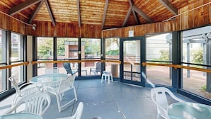 Une terrasse couverte avec des tables et des chaises en verre, des poutres en bois au plafond et de grandes fenêtres.