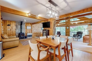 A wooden interior with a dining table, chairs, a sofa, a fireplace, and a television. - Stunning lakefront home with private dock, deck, firepit, and lake view (Wakefield)