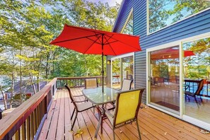 Eine Holzterrasse mit einem Glastisch und Stühlen, einem roten Sonnenschirm und einer Glasdoor zum Außenbereich.