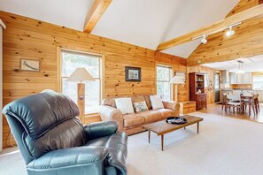 Ein Holzblockhaus-Interieur mit Ledersessel, Sofa, Esstisch und Küchenzeile.