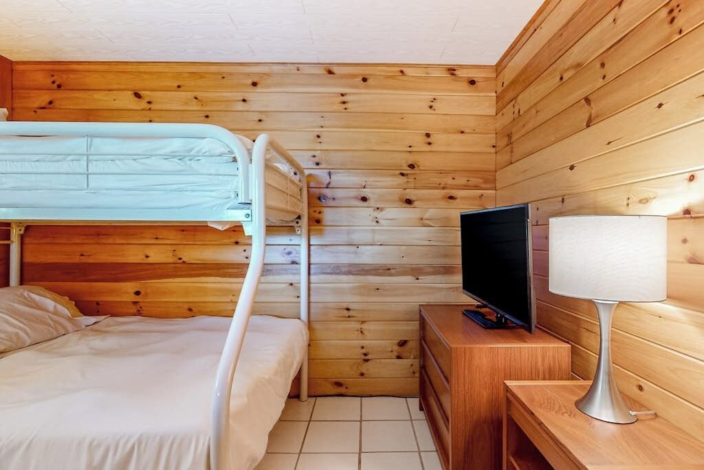 A wooden cabin room with a bunk bed, a television, and a bedside table.