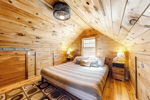 A cozy wooden cabin bedroom with a bed, nightstands, and a window. - Lakefront cottage with deck, patio, firepit, AC & W/D - secluded location (Wakefield)