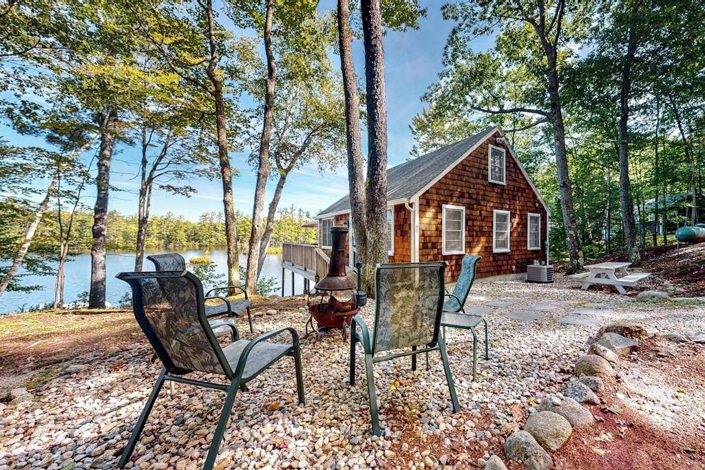 A cabin with a stone fireplace, surrounded by trees and a lake.