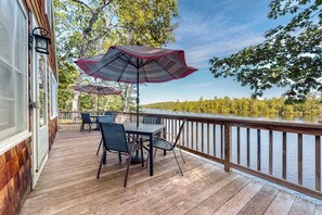 A wooden deck with outdoor furniture and umbrellas, overlooking a lake. - Lakefront cottage with deck, patio, firepit, AC & W/D - secluded location (Wakefield)