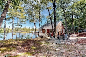 A cabin by a lake with a deck, chairs, and a small table. - Lakefront cottage with deck, patio, firepit, AC & W/D - secluded location (Wakefield)