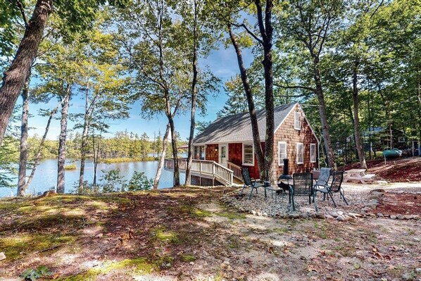 A cabin by a lake with a deck, chairs, and a small table. - Lakefront cottage with deck, patio, firepit, AC & W/D - secluded location (Wakefield)