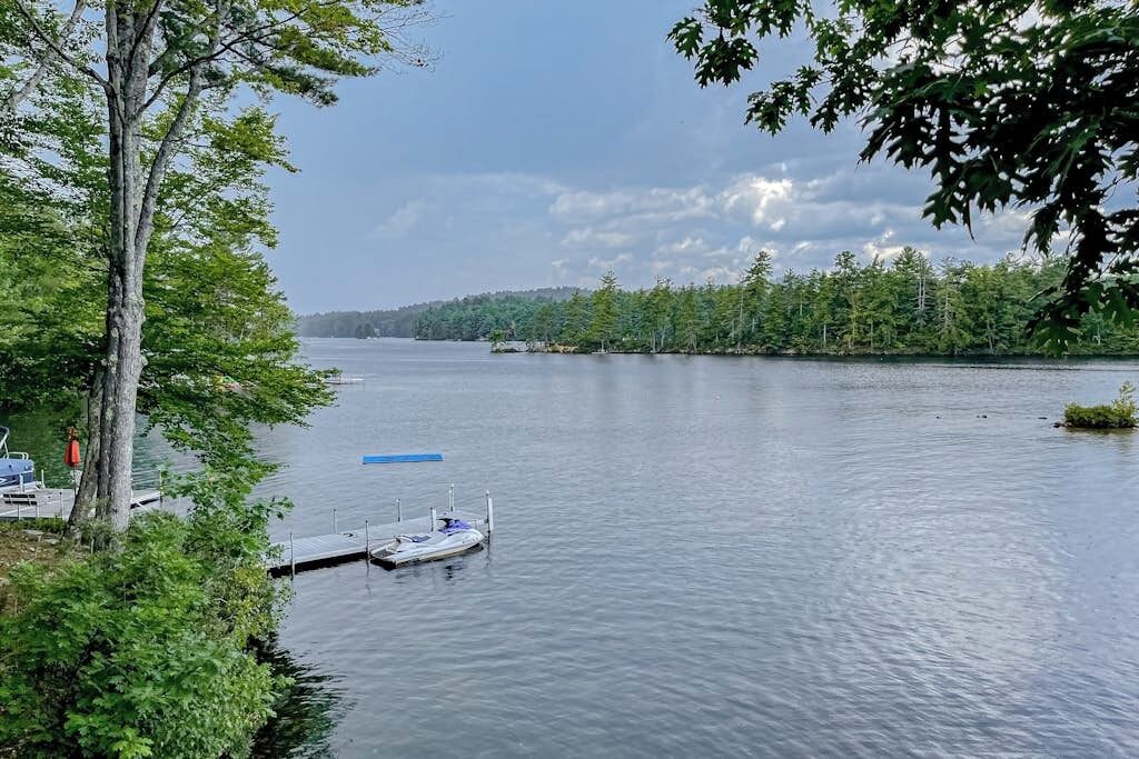 A calm lake with a dock and a boat, surrounded by dense trees.