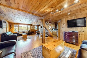 A spacious living area with wooden floors, a sofa, a coffee table, and a TV mounted on the wall. - Lakefront cottage with deck, patio, firepit, AC & W/D - secluded location (Wakefield)