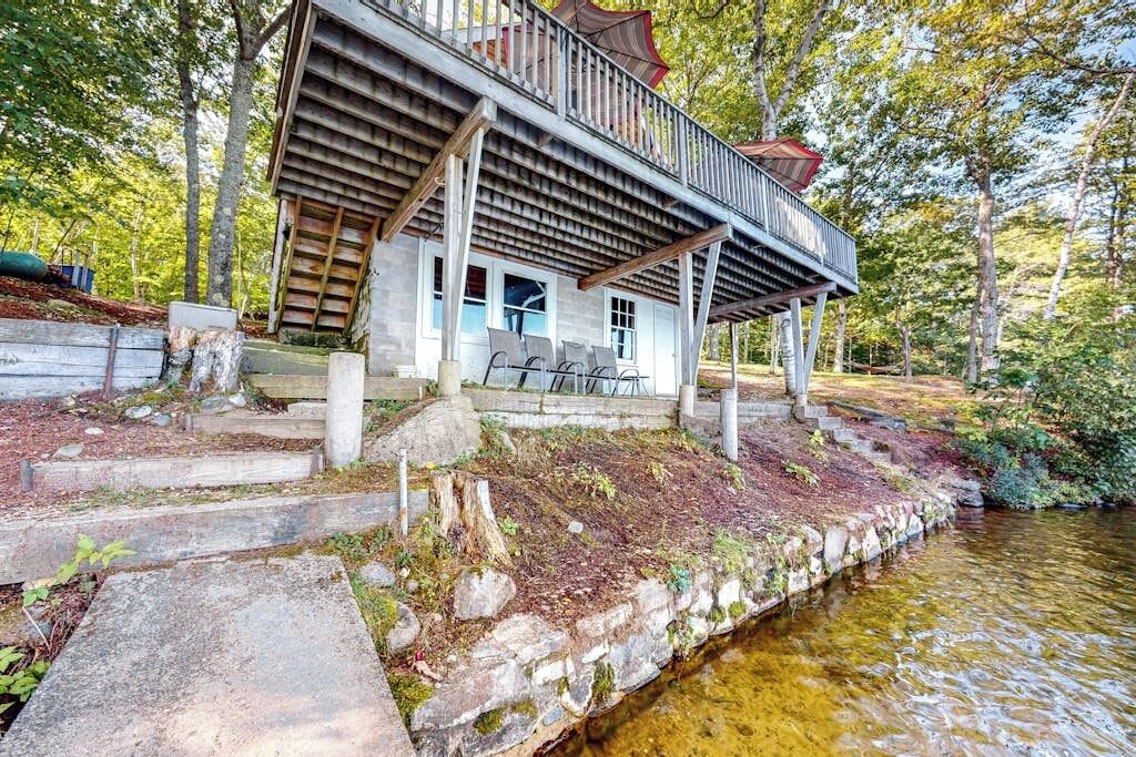 A cabin with a deck overlooking a stream, surrounded by trees.