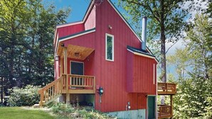 Una casa de madera roja con un balcón, una chimenea y una pequeña terraza.