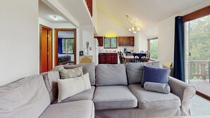 Una sala de estar con un sofá gris, armarios de madera y una zona de comedor con una mesa y sillas.