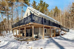 A cabin with a covered porch, a deck, and a steeply pitched roof.