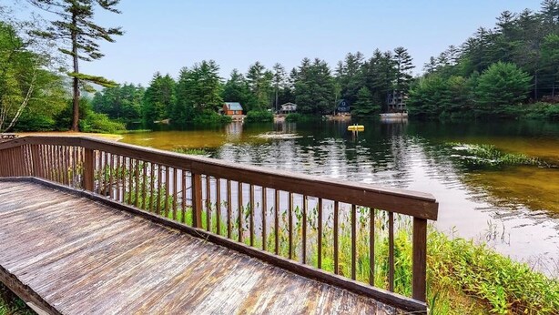 A wooden deck overlooking a calm lake with houses in the background. - Open concept home close to the beach with gas fireplace and deck (Madison)