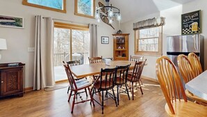 A dining area with a wooden table and chairs, a chandelier, and a kitchen area with a refrigerator. - Open concept home close to the beach with gas fireplace and deck (Madison)