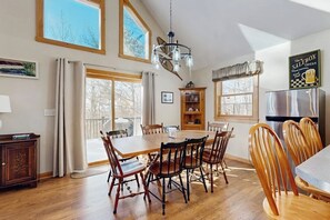 A dining area with a wooden table and chairs, a chandelier, and a kitchen area with a refrigerator.