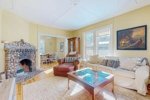 A living room with a stone fireplace, a glass coffee table, a white sofa, and a painting on the wall. - 2-story dog-friendly home in downtown with grill, mtn views, streaming, & porch (North Conway)
