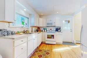 A compact kitchen with white cabinets, a microwave, an oven, and a window with a view of trees. - 2-story dog-friendly home in downtown with grill, mtn views, streaming, & porch (North Conway)