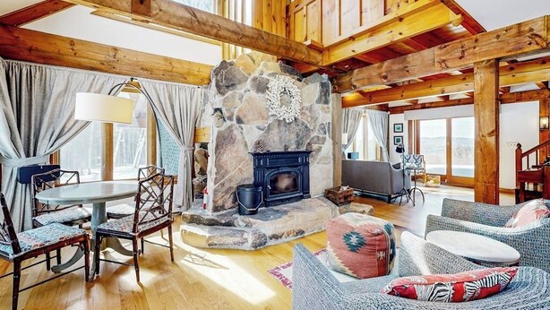 A spacious living room with a stone fireplace, wooden beams, a round table, and comfortable seating.