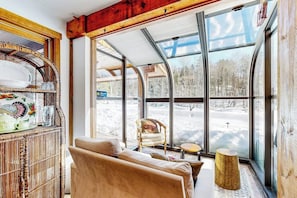 A cozy room with a large window, a wicker shelf, a sofa, and a small round table. - Stunning home with Moore Reservoir views and private sunroom (Littleton)