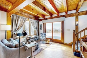 A spacious living room with a wooden ceiling, a sofa, a coffee table, a lamp, a chair, and a view through a glass door. - Stunning home with Moore Reservoir views and private sunroom (Littleton)