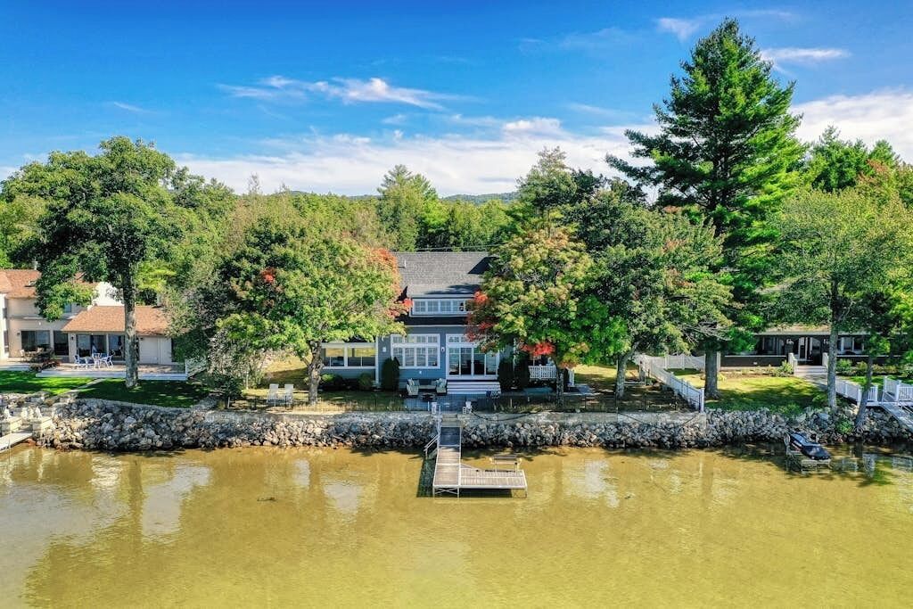 A lakeside property with a dock, a house with a sloped roof, and surrounding trees.