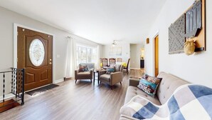 Amplia sala de estar con puerta de madera, un sofá y una zona de comedor con sillas.