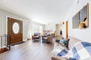 A spacious living room with a wooden door, a sofa, and a dining area with chairs. - Homey lakeside property w/ one house, two cottages, mtn. views, & private beach (Ossipee)