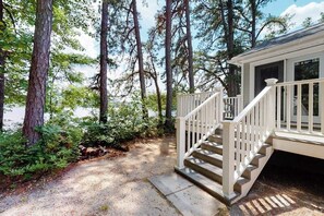 A wooden staircase leading to a house with a deck, surrounded by trees and a gravel path. - Homey lakeside property w/ one house, two cottages, mtn. views, & private beach (Ossipee)