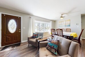 A living room with a sofa, armchair, dining table, and chairs. - Homey lakeside property w/ one house, two cottages, mtn. views, & private beach (Ossipee)