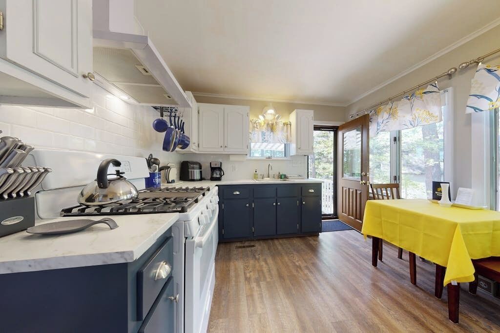 A modern kitchen with white cabinets, a stove, and a dining area with a yellow tablecloth.