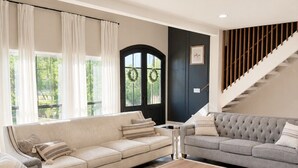 Un salon avec deux canapés, une table basse, un tapis à motifs, un escalier et une porte décorée de guirlandes.