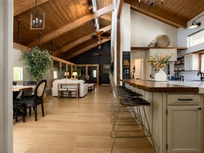 A spacious kitchen with wooden beams, a bar area, and a dining space with a large plant.