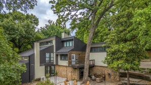 Une maison moderne à deux étages dotée d’un patio aménagé avec du mobilier d’extérieur et un mur en pierre.