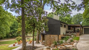 Une maison moderne avec une façade en pierre, un patio doté de mobilier d’extérieur et un jardin bien entretenu.