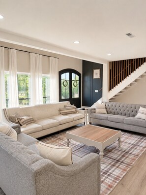 A living room with two sofas, a coffee table, a plaid rug, a staircase, and a door with wreaths. - Ultimate Family Retreat | Kids Loft + Firepit (Tulsa)