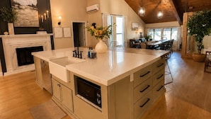 A spacious kitchen with a large island, wooden ceiling beams, and a dining area in the background. - Ultimate Family Retreat | Kids Loft + Firepit (Tulsa)